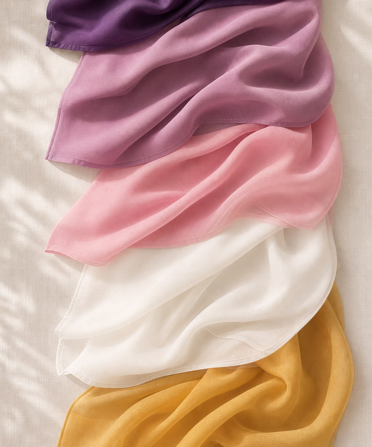 Stacked folded hijabs in plum, blush, ivory and gold